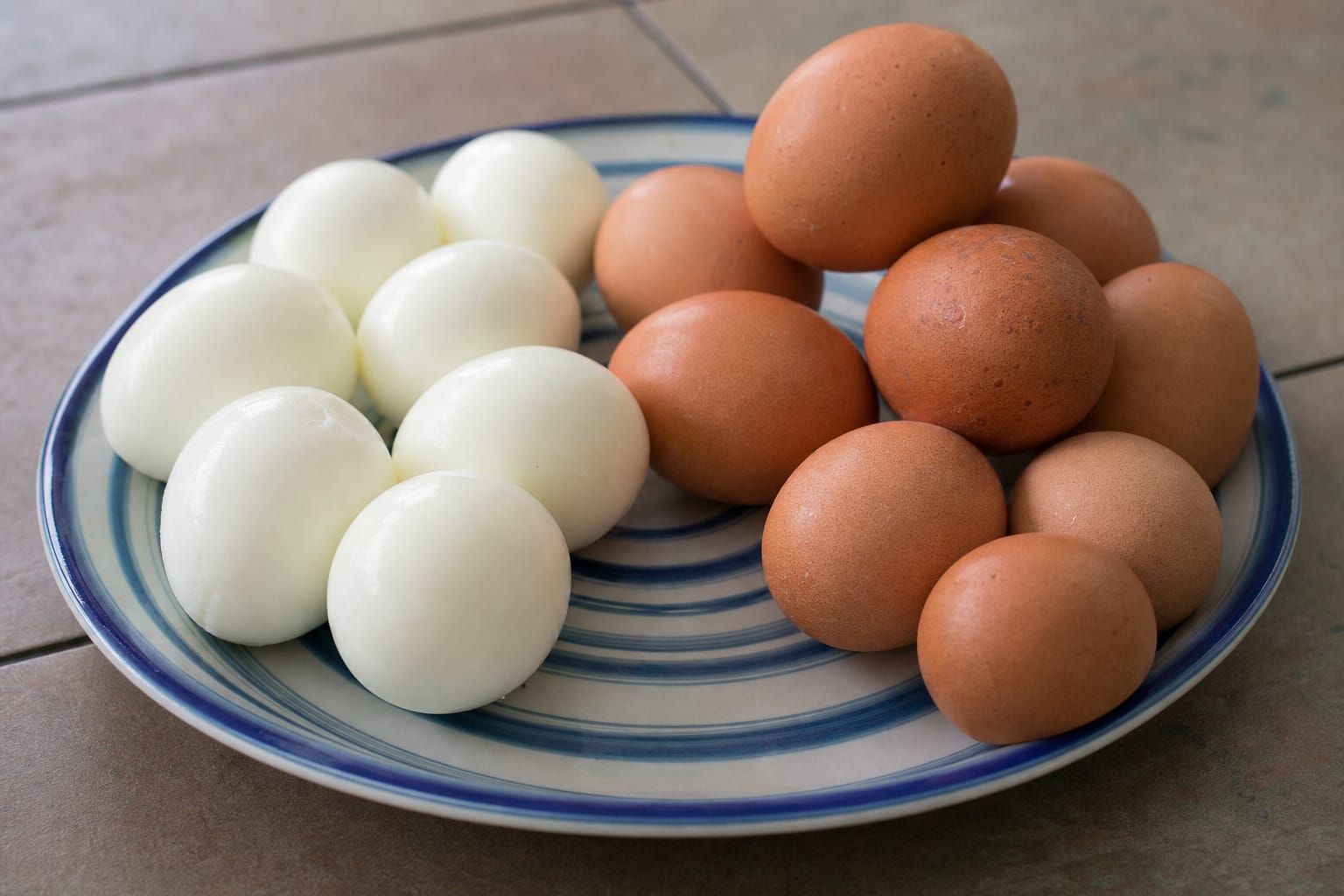 Oeufs durs écalés et non écalés posés côte à côte dans une assiette sur une table de cuisine