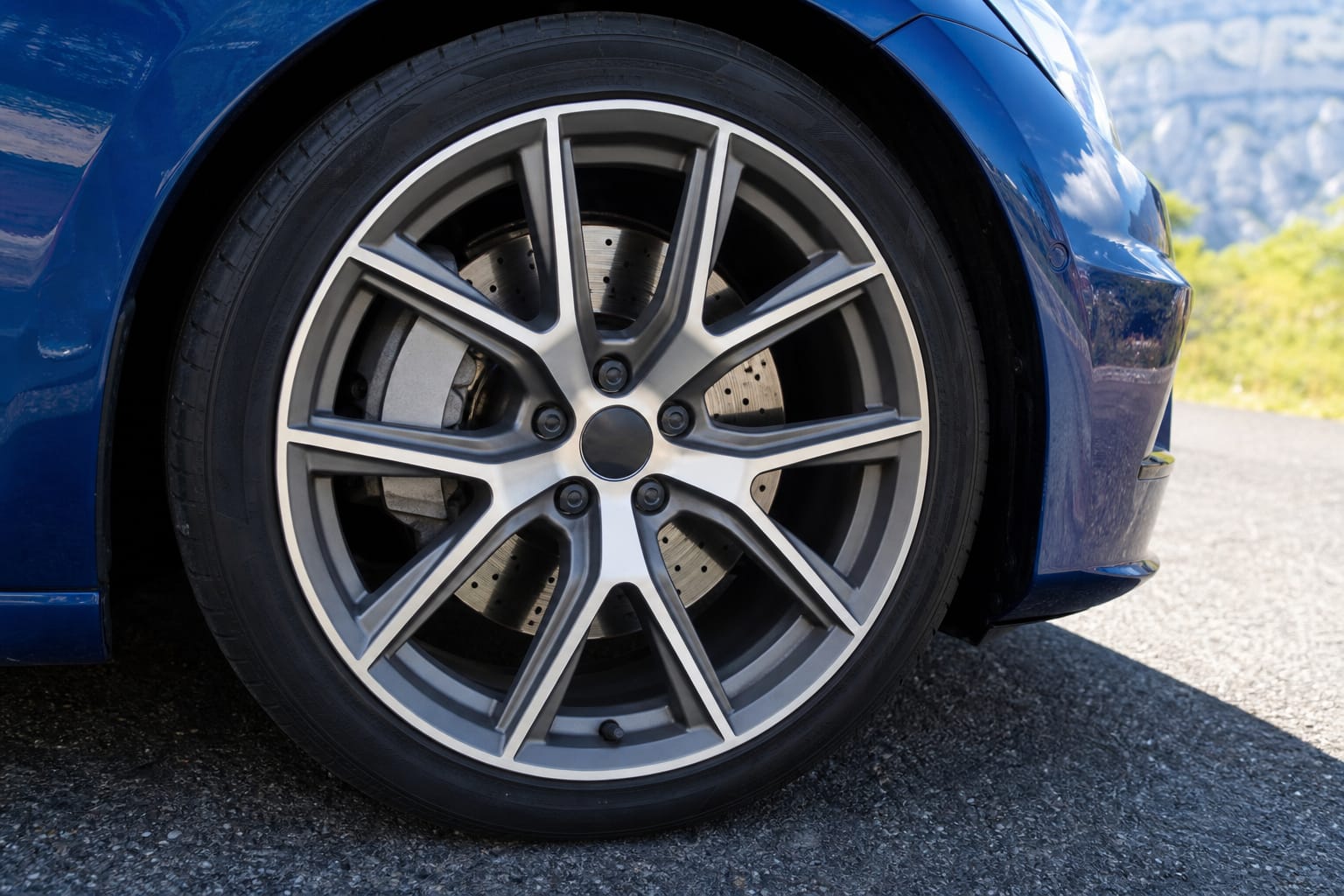 Roue avant de voiture avec disque de frein visible, vue en gros plan sur une route