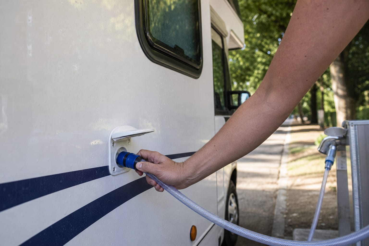 Main branchant un tuyau d'eau alimentaire sur la trappe de remplissage du réservoir d'eau propre d'un camping-car blanc sur une aire de services