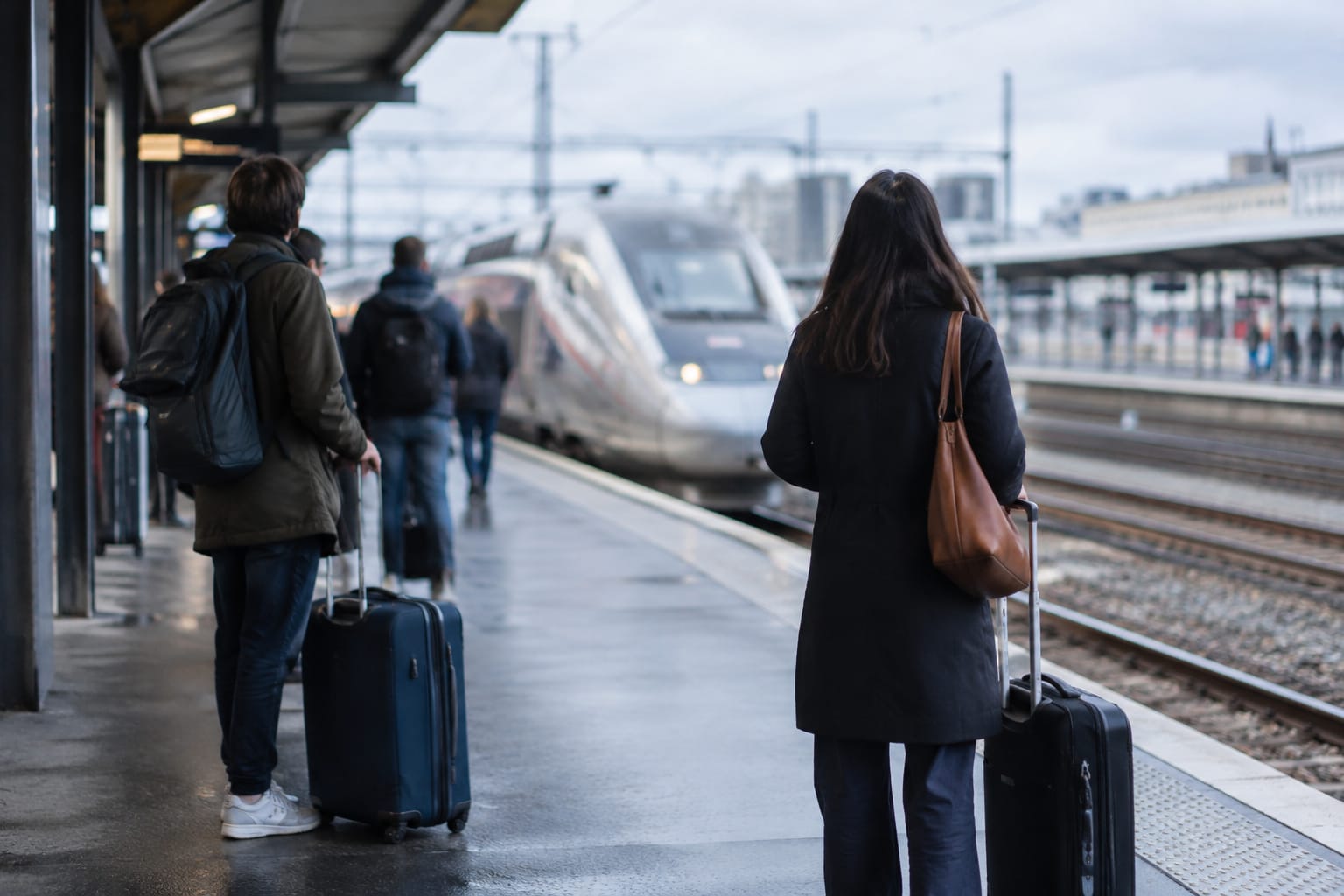 Voyageurs avec leurs valises attendant sur un quai de gare par temps gris, un train à grande vitesse flou en arrière-plan